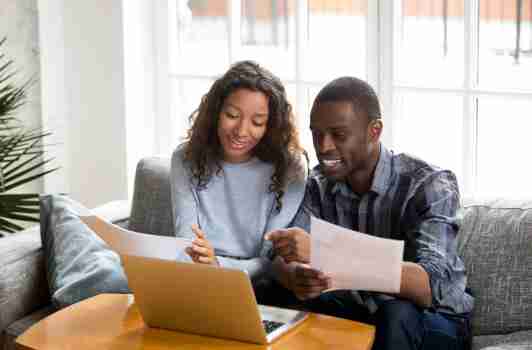 man and woman smiling, holding papers by a laptop