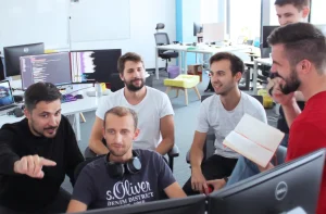 Image showing a group of developers gathered around a computer, discussing something.